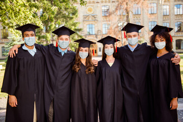 Photo of six successful young graduates wear black robes hats masks finished their education outside