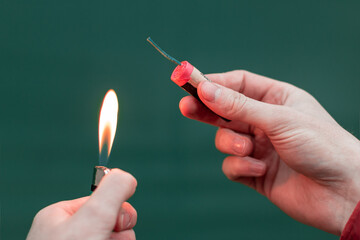 Man Lighting Up Firecracker in his Hand Against the Blue Background Using Gas Lighter