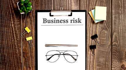 BUSINESS RISK word written on paper. On the background of accounting, pen and glasses.