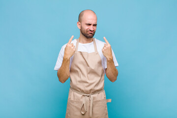 bald man with a bad attitude looking proud and aggressive, pointing upwards or making fun sign with...