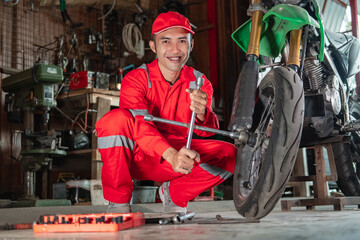side view of mechanic smiles at the camera while using wheel nuts to remove a motorcycle wheel in a repair shop