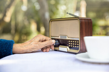 Senior woman hand turning knob on vintage radio in backyard.