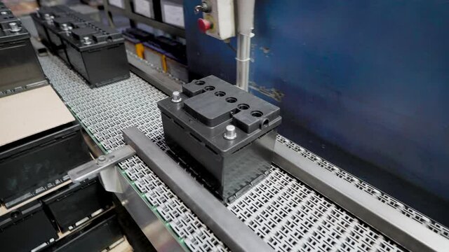 Automatic line for the assembly of car batteries. The black batteries move and collect on the conveyor belt.