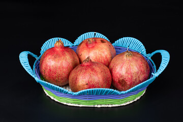 4 large red pomegranate on blue fruit basket on black background