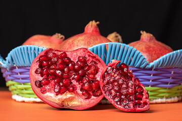 close up on pomegranate in fruit basket with half cut pomegranate and orange base