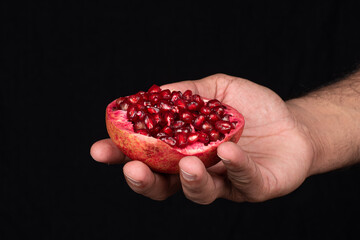 one half cut pomegranate in human hand against black background