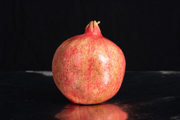one large red pomegranate on black surface with reflection