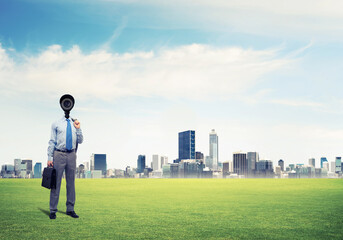 Camera headed man standing on green grass against modern cityscape