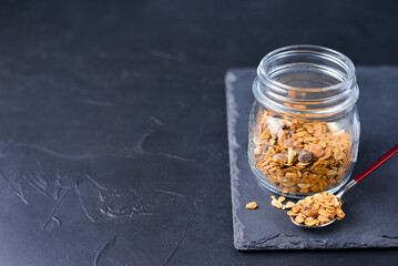 Crunchy honey homemade granola with nuts, berries, chocolate in a glass jar on a dark concrete...