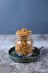 Crunchy honey homemade granola with nuts, berries, chocolate in a glass jar on a gray concrete background. Healthy vegan snack idea on breakfast. Copy space. Easy to cook recipe nutrition.