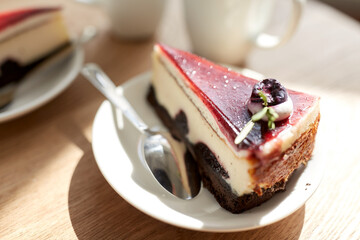 food, junk-food, culinary, baking and holidays concept - piece of delicious cherry chocolate layer cake on saucer with spoon on wooden table