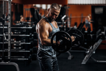 Muscular young man lifting weights in gym on dark background