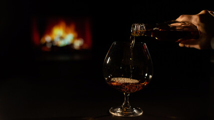 Close-up of a female hand with a glass of brandy on the background of the fireplace