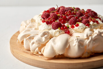food, culinary, baking and cooking concept - close up of pavlova meringue cake decorated with red berries on wooden serving board