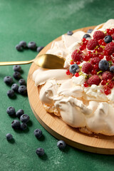 food, culinary, baking and cooking concept - close up of pavlova meringue cake decorated with berries on wooden serving board