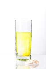 A large, white tablet with dissolves in a glass of water on a white background. Vitamin C.