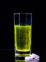 A large tablet dissolves in a glass of water on a black background.