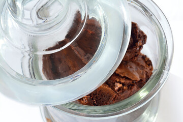 Close-up of a glass cookie jar filled with chocolate brownie pieces and the lid ajar. Top view.
