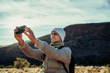 Young caucasian hiker taking selfie with smartphone while walking through luscious mountain 