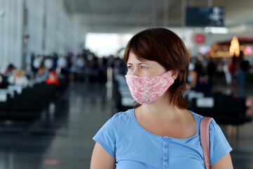 Woman in protective face mask standing in the airport terminal. Passenger are waiting for their flight, safety measures during the covid-19 coronavirus pandemic