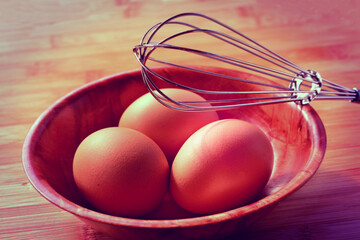 Retro style photo of three brown eggs in a bowl and a wire whisk. Toned image.