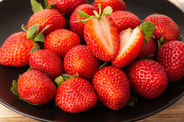 Ripe red strawberries and two sliced strawberry slices on top on a black plate close-up.