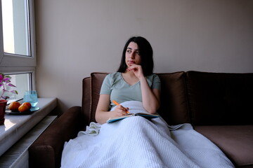 The corona patient lying on the sofa takes notes in her notebook. spending time in quarantine.