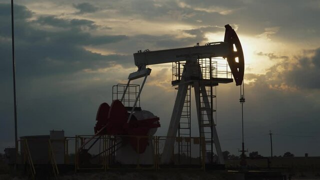 Oil mining, an oil rig in the field pumps out oil, view of an oil rig at sunset, resource extraction for fuel production, sunset light in the golden hour.
