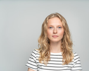 Beautiful young serious clever blonde woman without makeup on white wall. Pretty female with curly hair in white t shirt