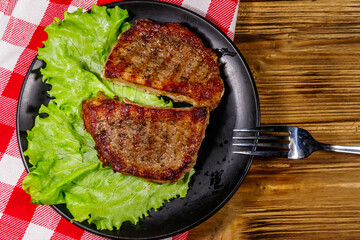 Grilled pork steaks with lettuce leaves on wooden table. Top view