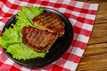 Grilled pork steaks with lettuce leaves on wooden table