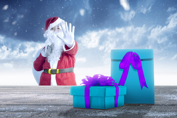 Asian man in Santa costume with an open hand carrying gift bag with gift box on wooden table