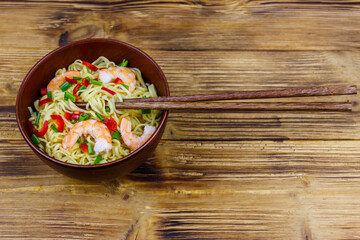 Bowl of instant Chinese noodles with shrimps, green onion and red hot chilli peppers on wooden table. Top view