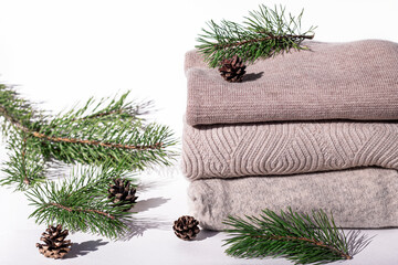 Stack of pastel color winter knitted sweaters, fir cones and fir tree branch on white background. Cozy Autumn and winter concept