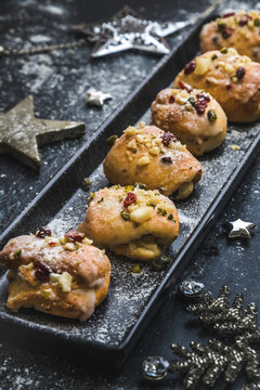 Homemade mini stollen with icing, dried cranberries and pistachios on a black tray on a black background, decorated with silver stars. Vertical stock photo.