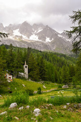 Fototapeta na wymiar A small stone church in a pine forest at the foot of the Mont Blanc massif in a cloudy summer day, Ferret Valley, Courmayeur, Aosta Valley, Alps, Italy