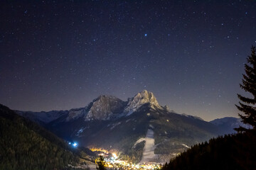 Fototapeta na wymiar Dolomites by nightSky with stars on a winter night in val di fassa. Dolomites, forest and night lights of Pozza di Fassa