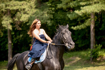Girl with a long copper hair and long flowy shoulderless dress,  ride a black horse with trees in the background.