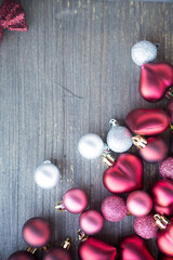 Vertical picture with small red and silver decorations for Christmas tree in bottom right corner. Copy space. New year hearts and balls on wooden grey surface. Flat layer composition for winter