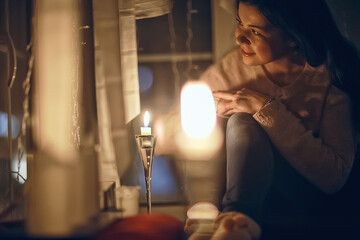 Christmas evening girl / beautiful young adult model, dreams and makes wishes at the candles in the...