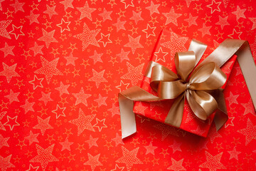 Red Christmas gift with golden ribbon and bow on red background decorated with golden stars...