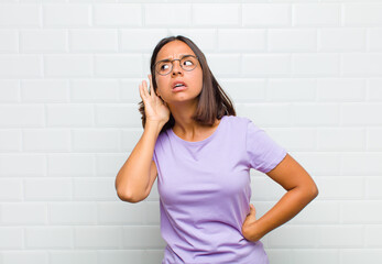 latin woman looking serious and curious, listening, trying to hear a secret conversation or gossip,...