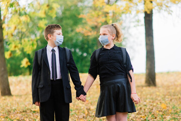 Schoolchildren, a boy and girl in medical masks walk in the city park.