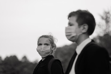 Schoolchildren, a boy and girl in medical masks walk in the city park.