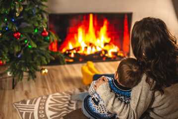 Mom and little son are sitting in an embrace next to the fireplace. Concept of creating a cozy winter atmosphere at home