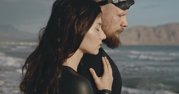 ouple standing on the ocean. Cinematic shot, perfect girl looking into distance. Man and woman in black suits in beautiful landscape by the water. Thoughtful look. People supporting each other.