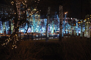 Night city street with New Year's illumination and tree trunks illuminated by bulbs