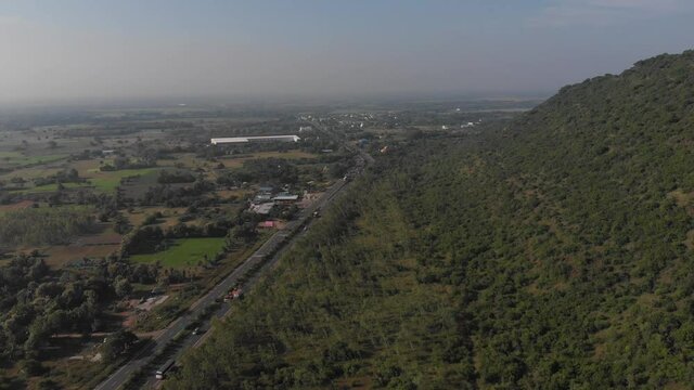 Looking down at Tindivanam Highway from far above a forested hillside at midday