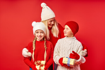 Fototapeta premium pretty woman and happy children celebrate Christmas together, hold gifts in hands, smile, isolated on red studio background. real happy emotions