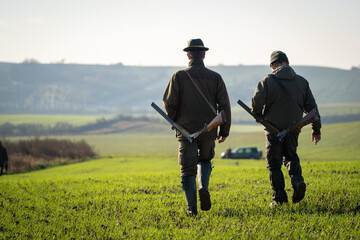Couple of gamekeepers walk over cultivated field looking for a prey.